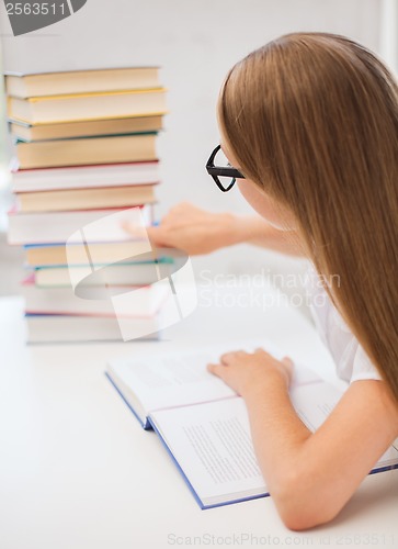 Image of little student girl in eyeglasses with many books