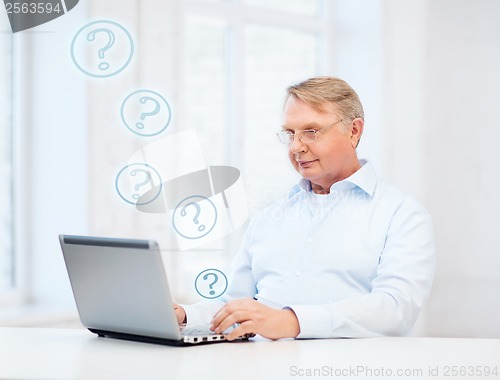 Image of old man in eyeglasses working with laptop at home