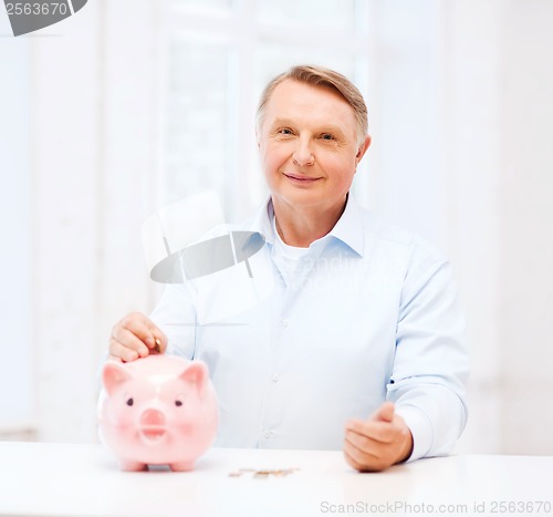 Image of old man putting coin into big piggy bank