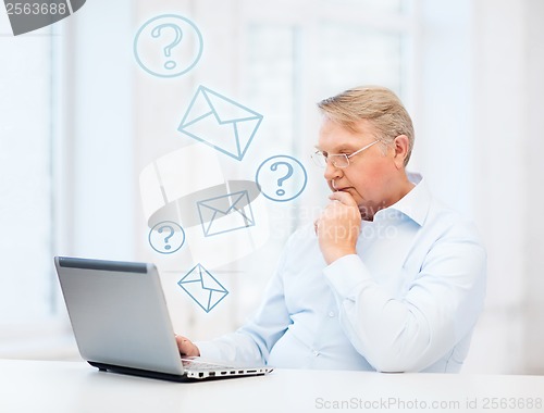 Image of old man in eyeglasses working with laptop at home