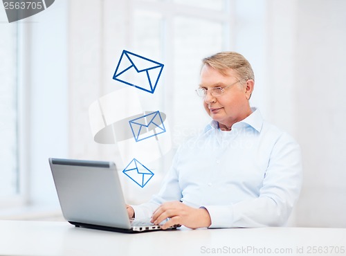 Image of old man in eyeglasses working with laptop at home