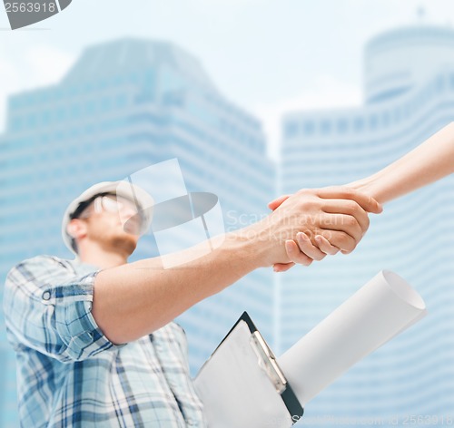 Image of builder with blueprint shaking partner hand