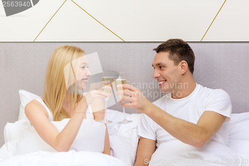 Image of smiling couple with champagne glasses in bed