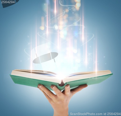 Image of hand holding open book with magic lights