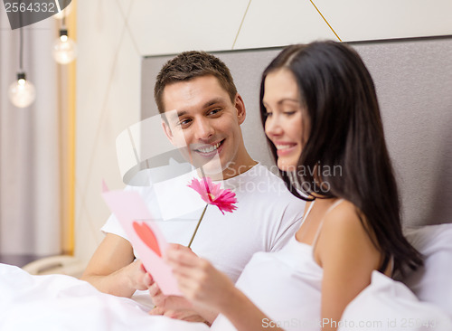 Image of smiling couple in bed with postcard and flower