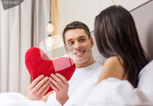 Image of smiling couple in bed with red heart shape pillow