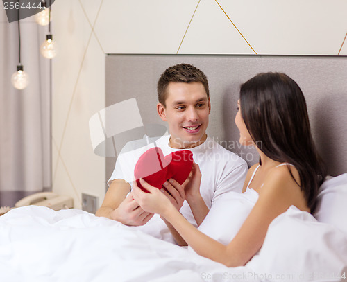 Image of smiling couple in bed with red heart shape pillow