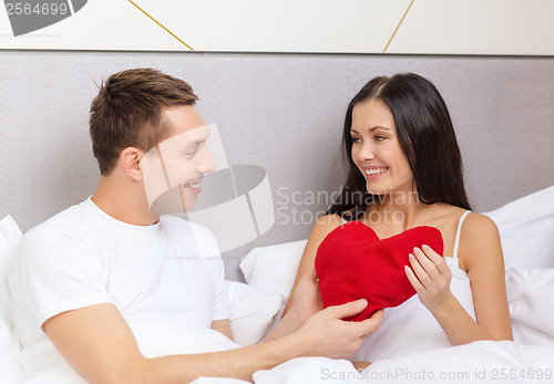 Image of smiling couple in bed with red heart shape pillow