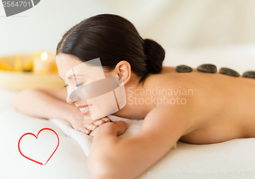 Image of smiling woman in spa salon with hot stones