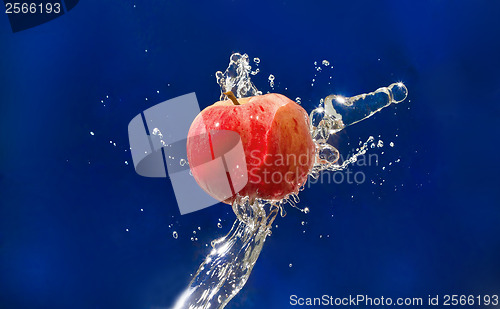 Image of Red Apple drops in the jet of water sprays on blue texture
