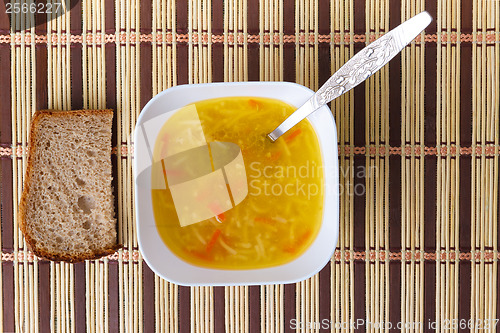 Image of soup of bowl with a spoon and bread on the mat