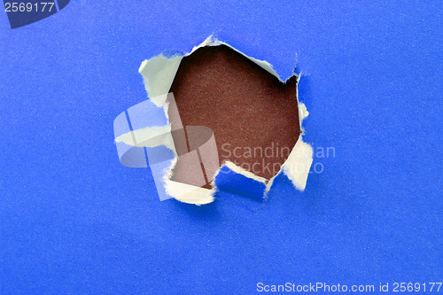 Image of hole in the blue paper with ragged edges and brown texture