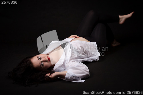 Image of Portrait of long-haired woman in men's shirt lying on a black ba