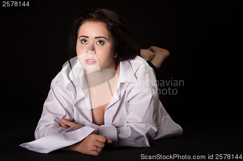 Image of Portrait of long-haired woman in men's shirt lying on a black ba
