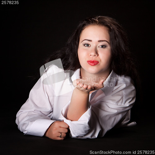 Image of Portrait of long-haired woman in men's shirt lying on a black ba