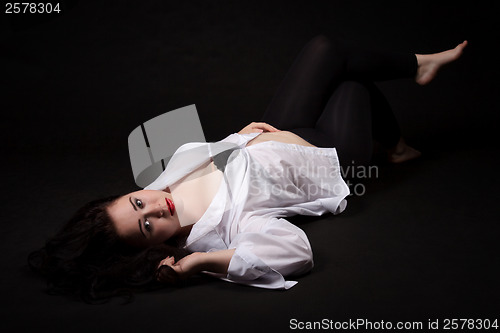 Image of Portrait of long-haired woman in men's shirt lying on a black ba