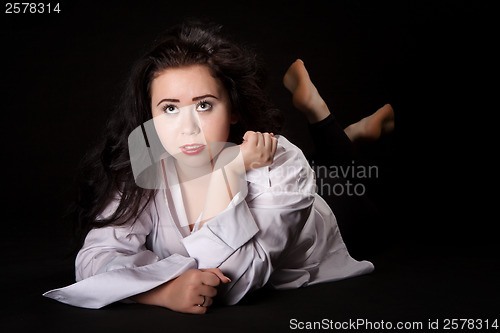 Image of Portrait of long-haired woman in men's shirt lying on a black ba