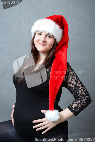 Image of beautiful pregnant santa woman tenderly holding her tummy