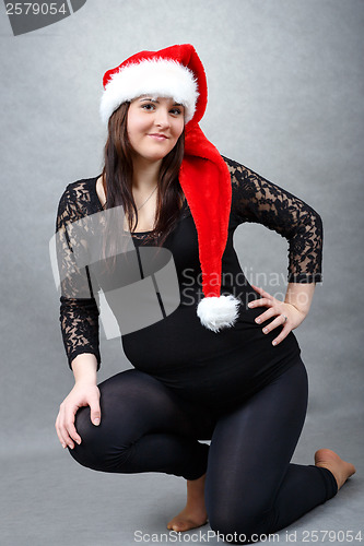 Image of beautiful pregnant santa woman tenderly holding her tummy
