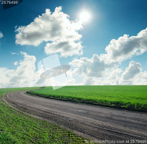 Image of road in green grass under cloudy sky with sun