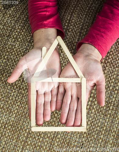 Image of Hands holding model house made of wooden sticks