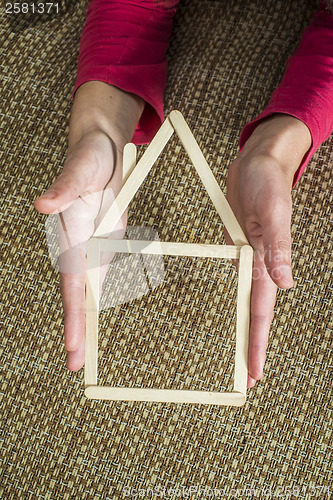 Image of Hands holding model house made of wooden sticks