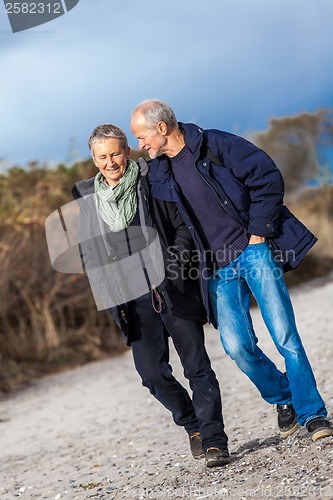 Image of mature senior couple walking on the beach autumn winter