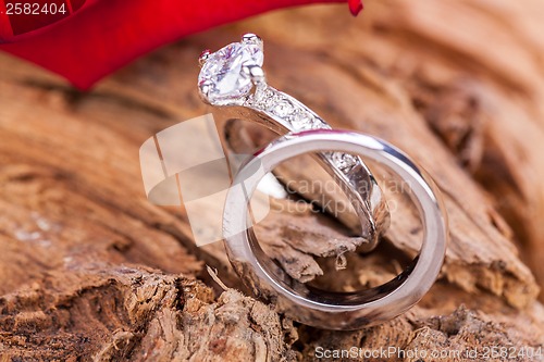 Image of beautiful ring on wooden background and red rose