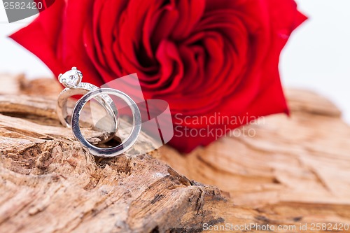 Image of beautiful ring on wooden background and red rose