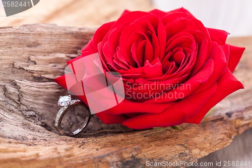 Image of beautiful ring on wooden background and red rose