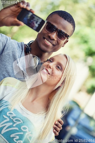 Image of young smiling multiracial couple taking foto by smartphone 