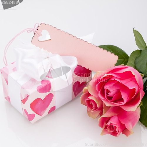 Image of Gift box with an empty tag, next to three roses