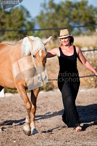 Image of young woman training horse outside in summer