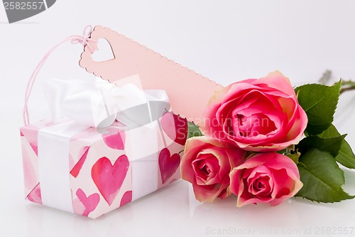 Image of Gift box with an empty tag, next to three roses