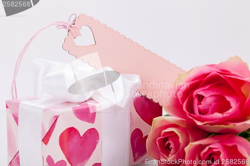 Image of Gift box with an empty tag, next to three roses