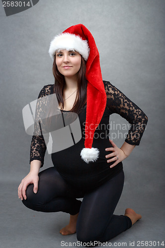 Image of beautiful pregnant santa woman tenderly holding her tummy