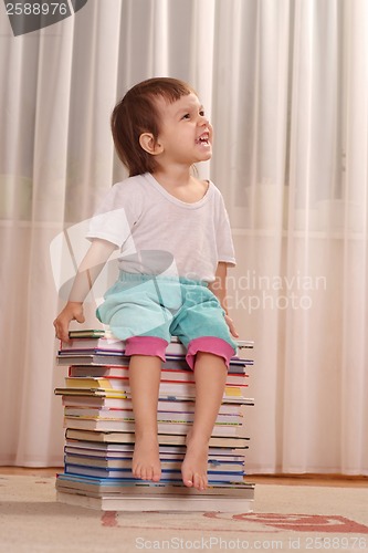 Image of Little Caucasian girl sitting on a pile of books