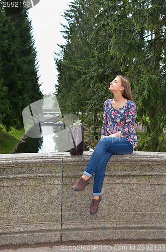 Image of eautiful girl sits on an old stone bridge 