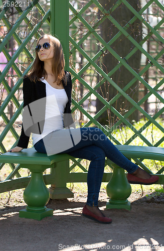 Image of portrait of the beautiful girl sits on a bench in green park