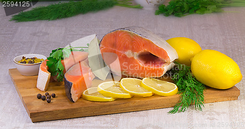 Image of Fish salmon, lemon and greens placed on the table.