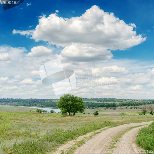 Image of dirty road in green meadow and clouds over it