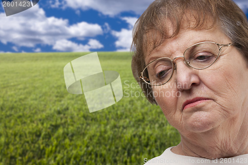 Image of Melancholy Senior Woman with Grass Field Behind