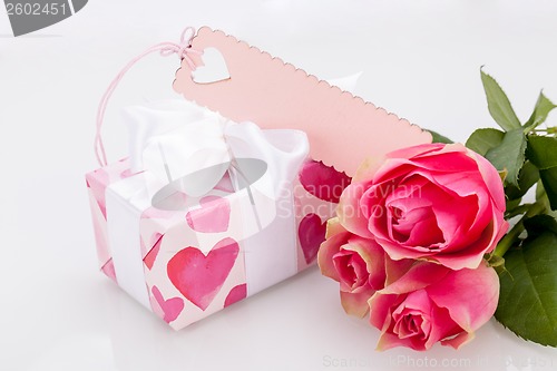 Image of Gift box with an empty tag, next to three roses