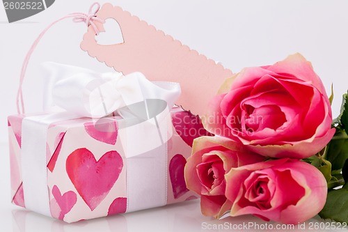 Image of Gift box with an empty tag, next to three roses