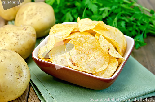 Image of Chips in a bowl with a potato on the board and napkin