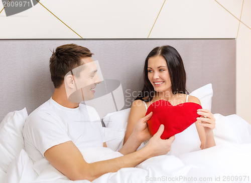 Image of smiling couple in bed with red heart shape pillow