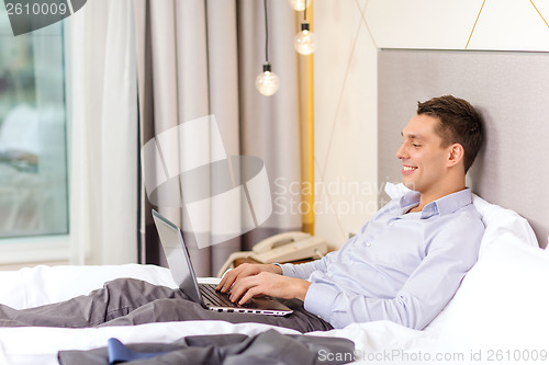 Image of happy businesswoman with laptop in hotel room