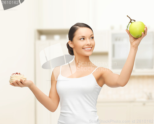 Image of sporty woman with apple and cake in kitchen