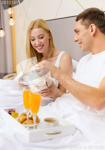 Image of smiling couple having breakfast in bed in hotel