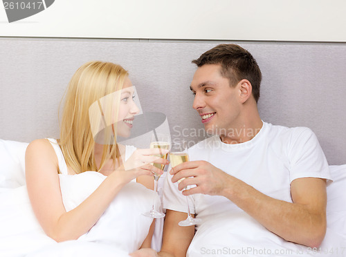 Image of smiling couple with champagne glasses in bed
